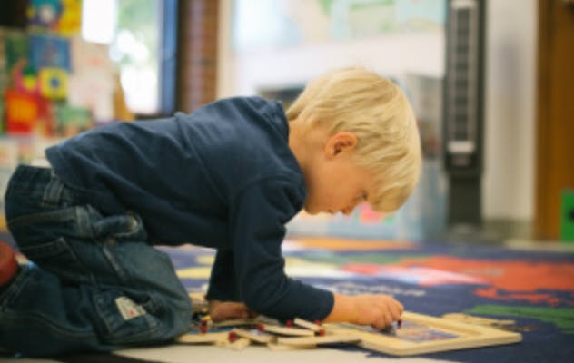 Child kneeling on floor playing with a puzzle
