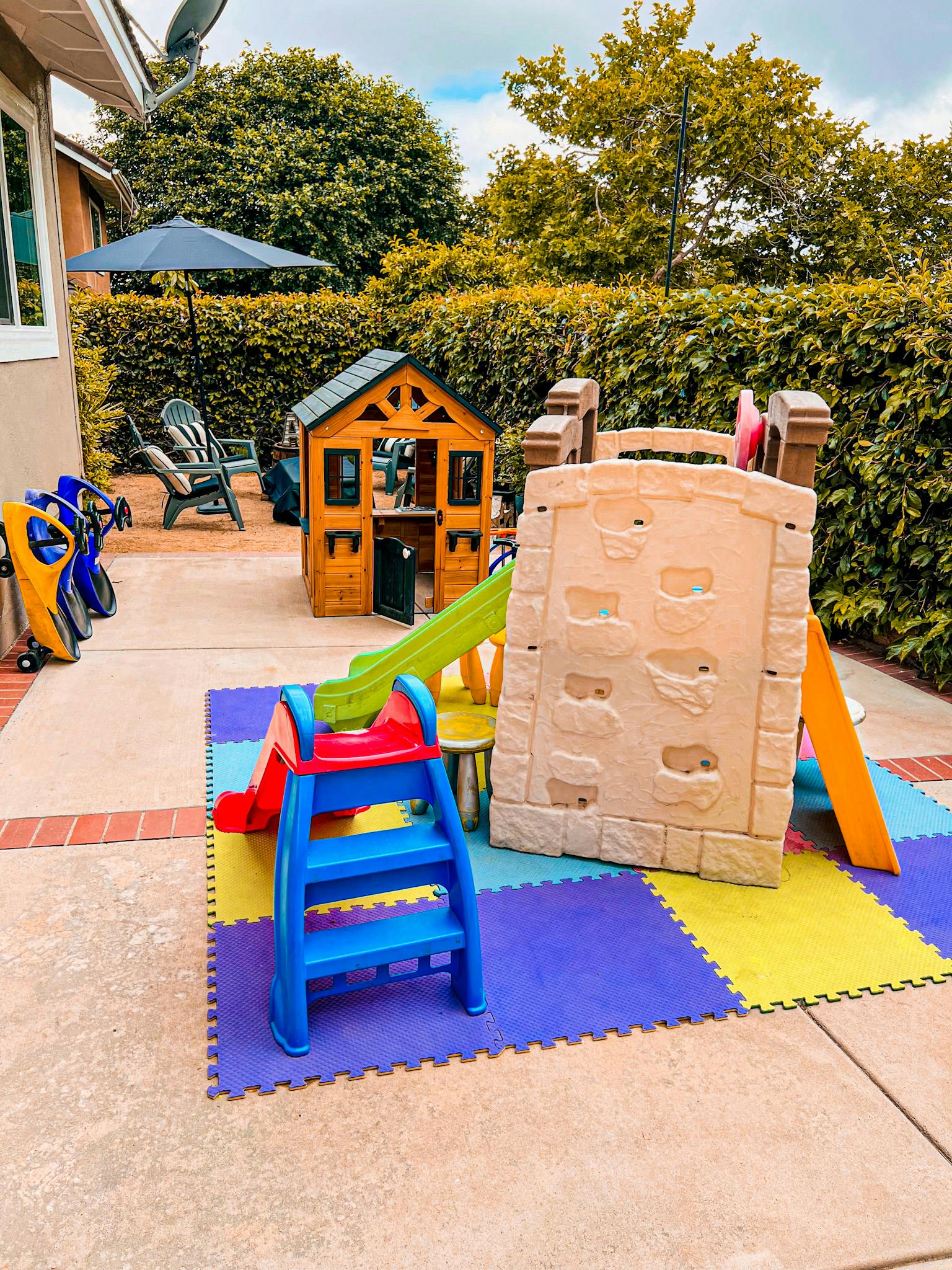 Outdoor play area with a wooden playhouse, slides, and climbing wall