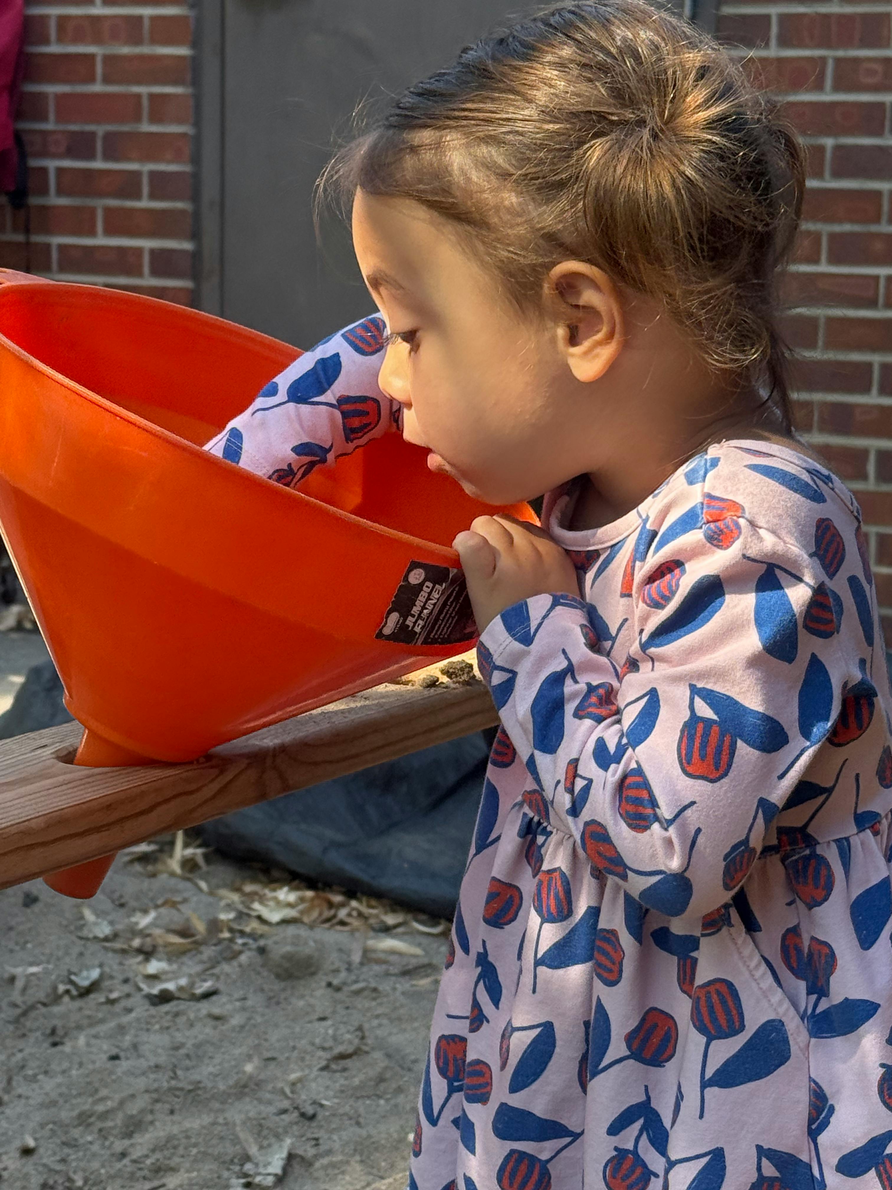 Child looking into an orange funnel on a wooden plank