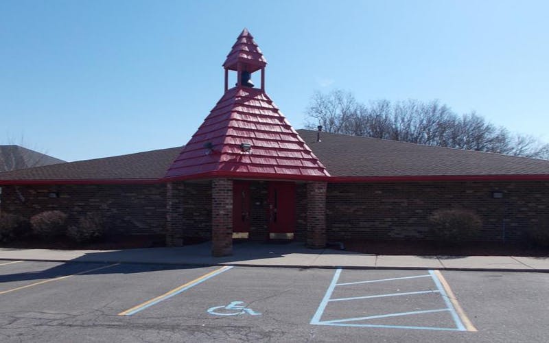 Brick building with a red-shingled steeple and a paved parking lot in front