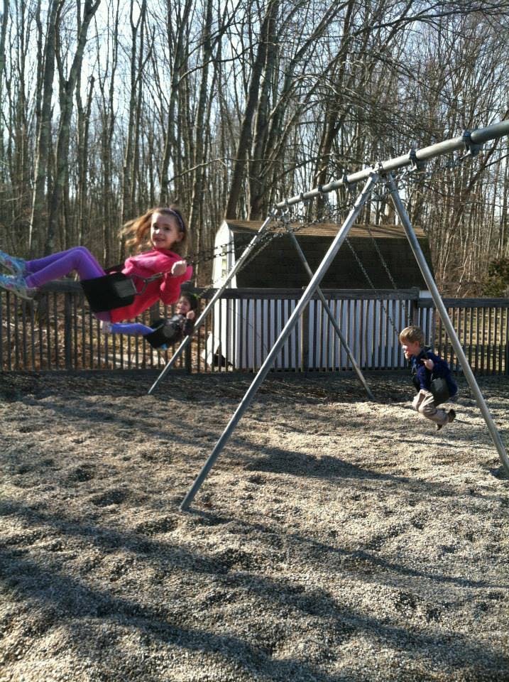 Child swinging on a swing set, another child in the background