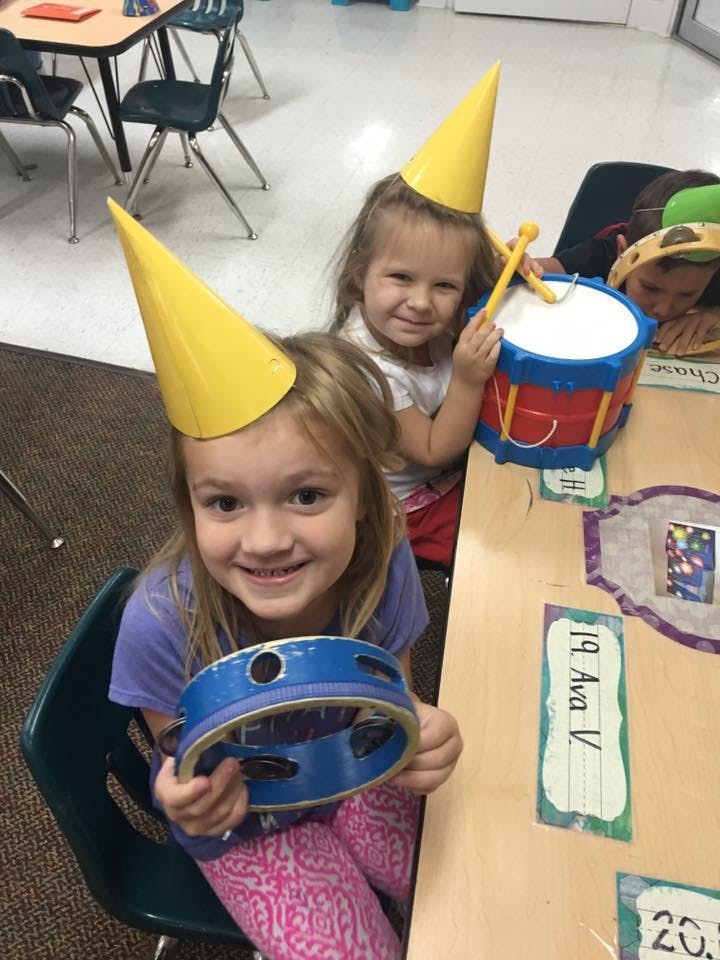 Two children wearing party hats, one holding a tambourine and the other a drum