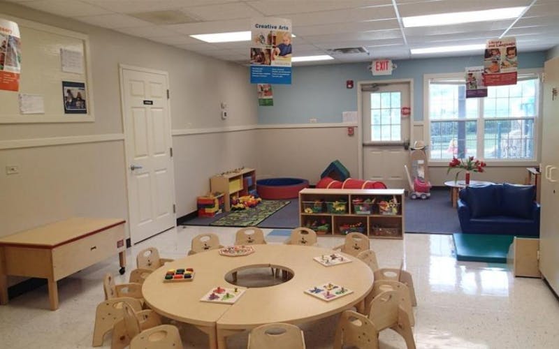 Classroom with child-sized tables and chairs, play area with toys and tunnel