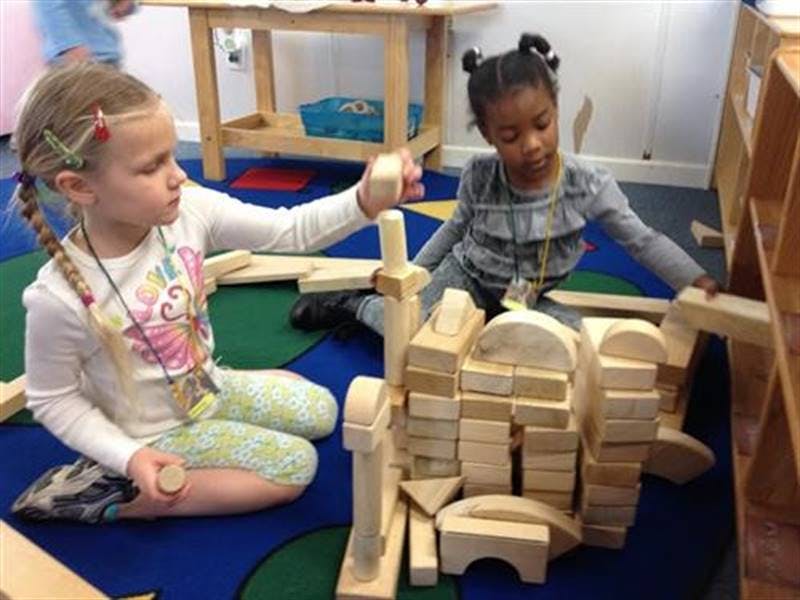 Two children playing with wooden blocks on a colorful rug