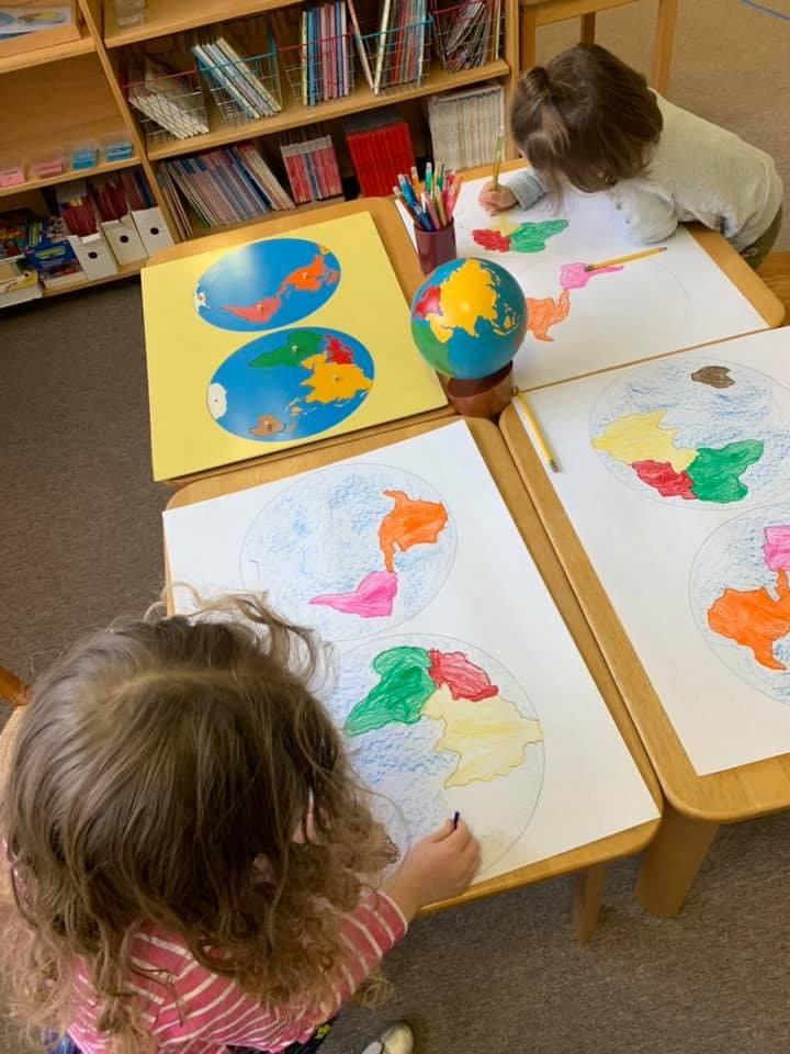 Two children coloring world maps at a table with a globe