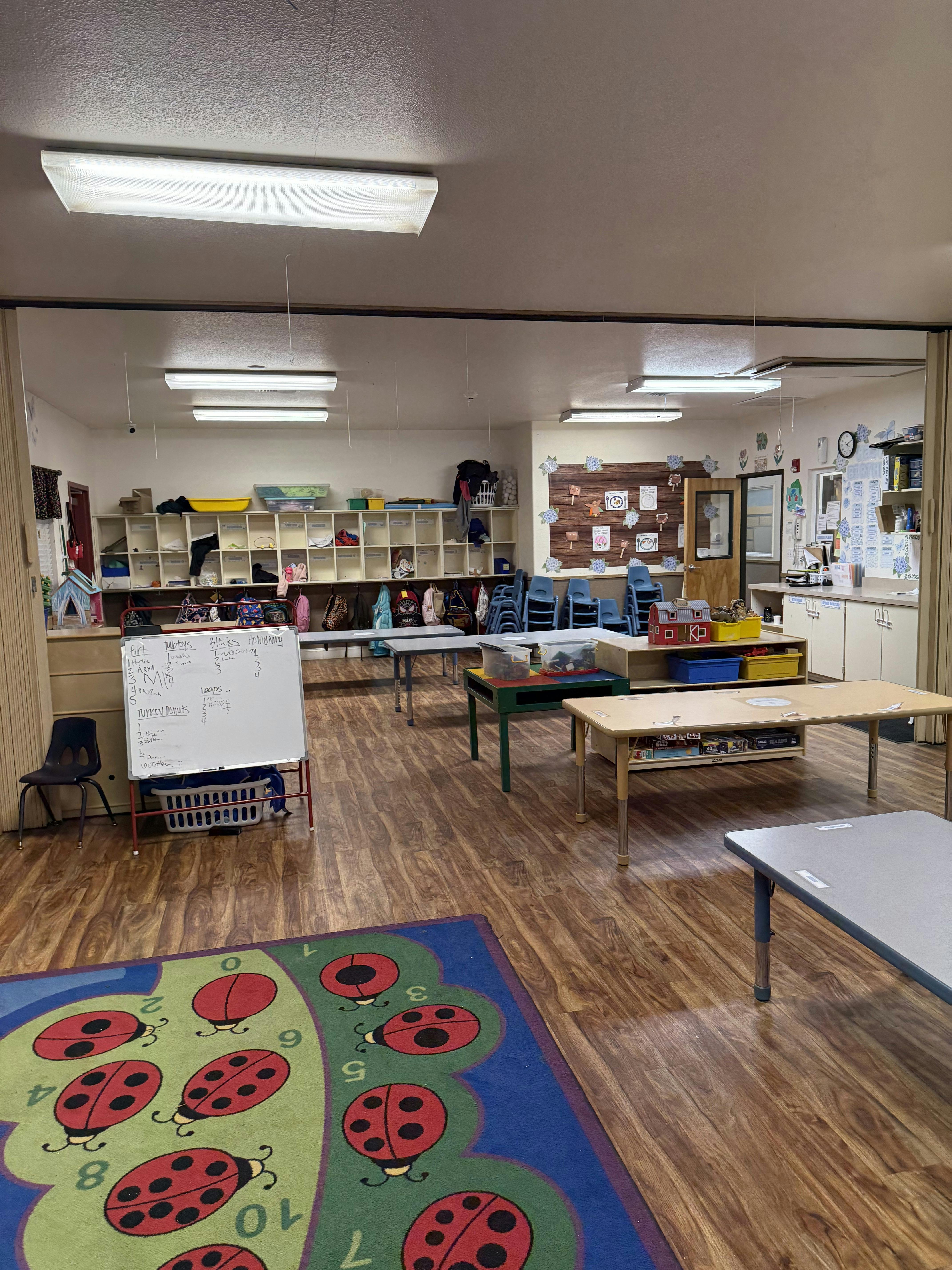 Empty classroom with tables, chairs, storage cubbies, and a ladybug rug
