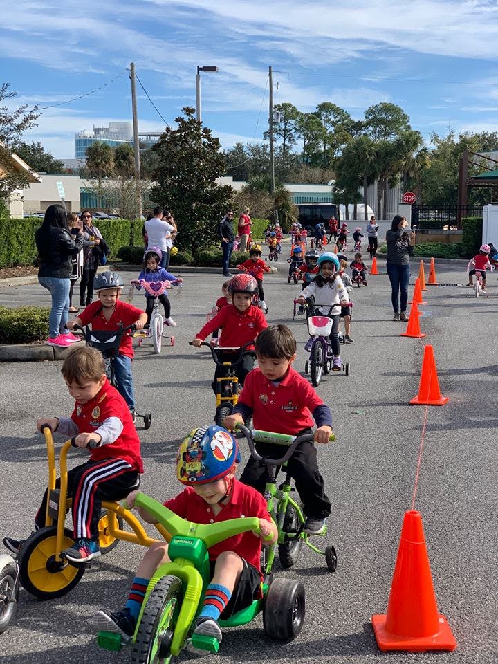 Children on tricycles and bicycles on a paved surface with orange cones