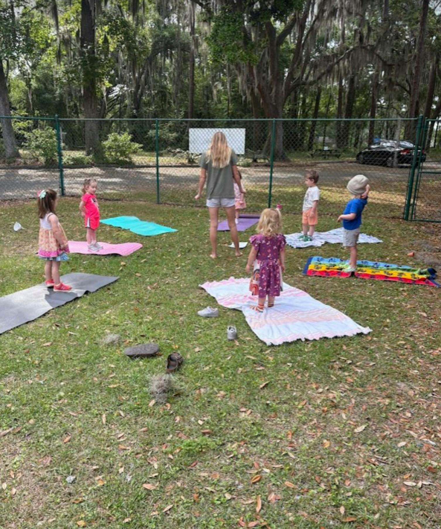Person leading children in an outdoor activity on mats