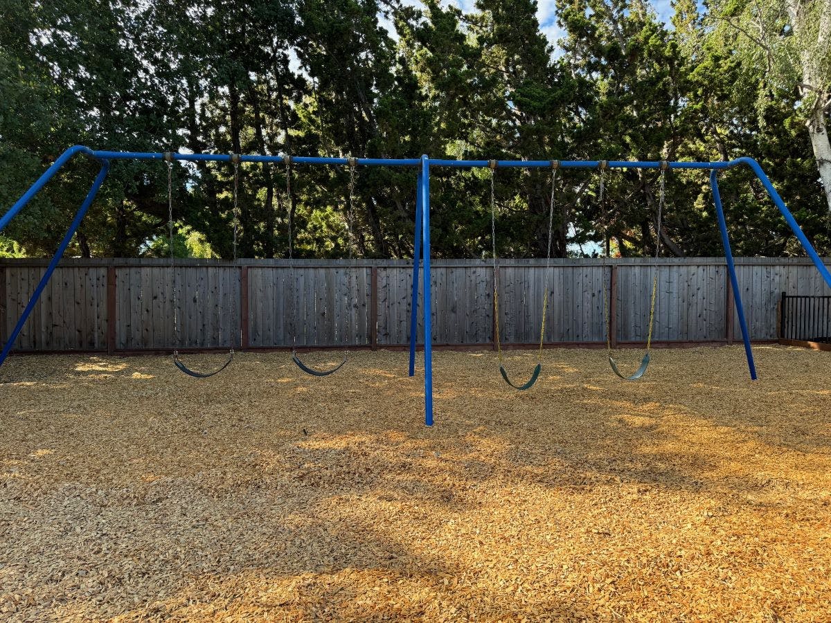 Empty blue swing set on a playground with wood chips