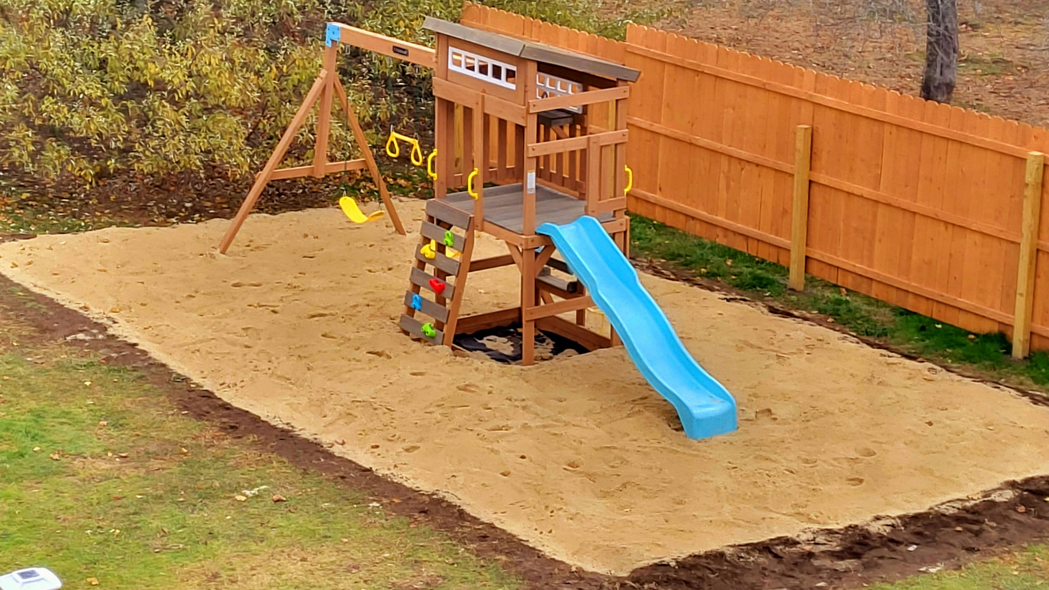 Wooden playground set with a blue slide and swings on a sand base
