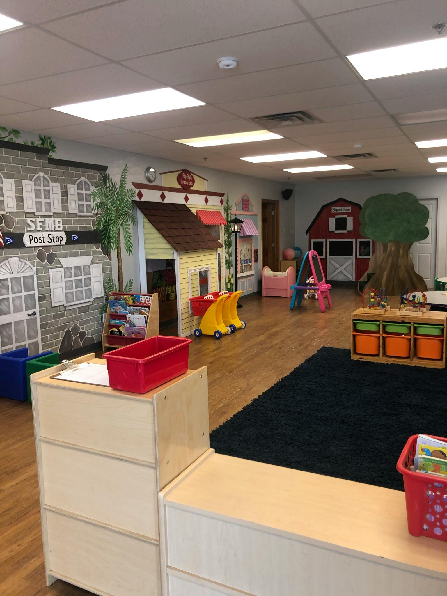 Playroom with toy houses, a tree, and a black rug