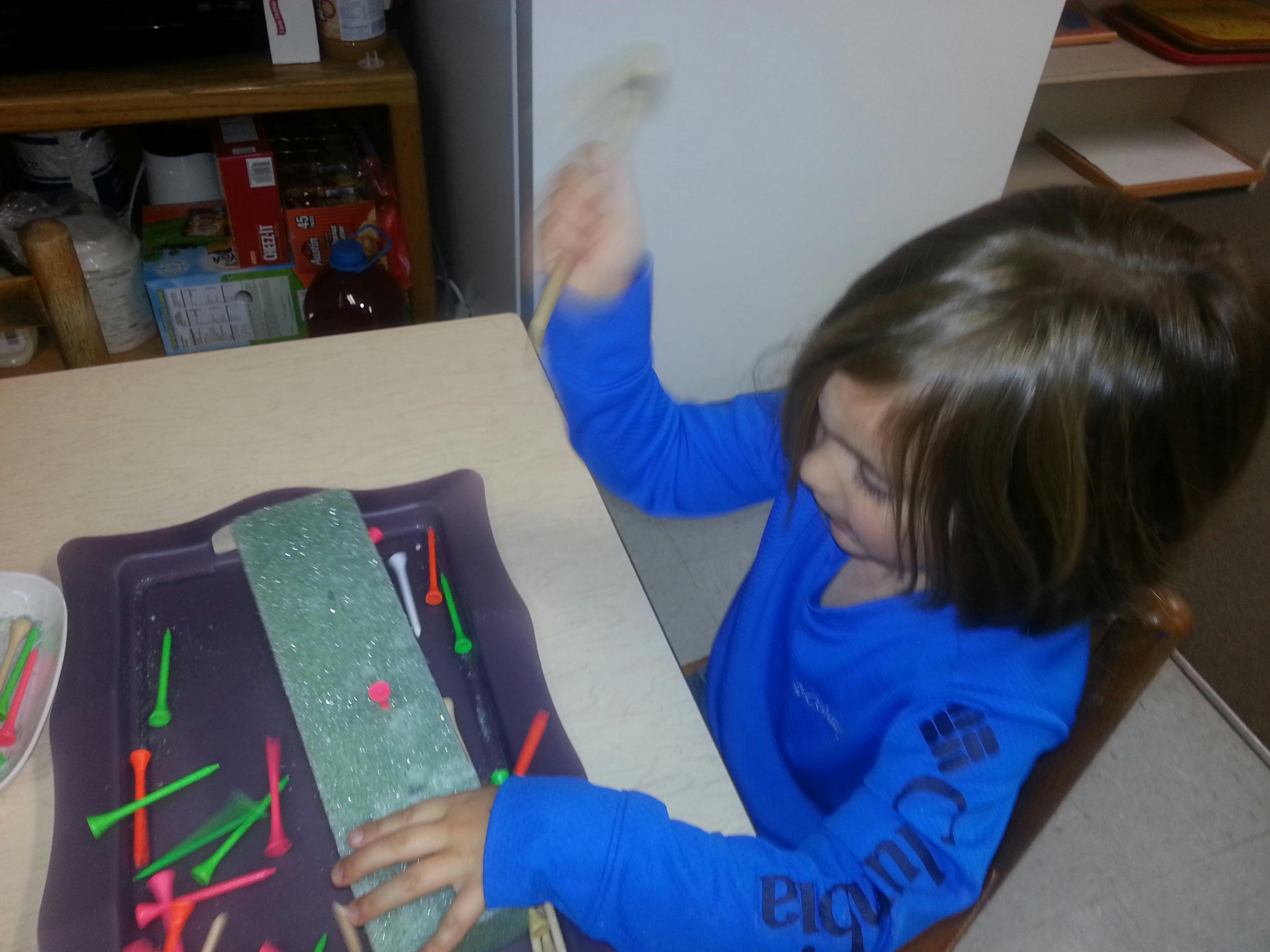 Child playing with golf tees and a green block on a tray