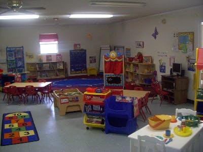 A brightly lit classroom with small tables, chairs, and various learning materials