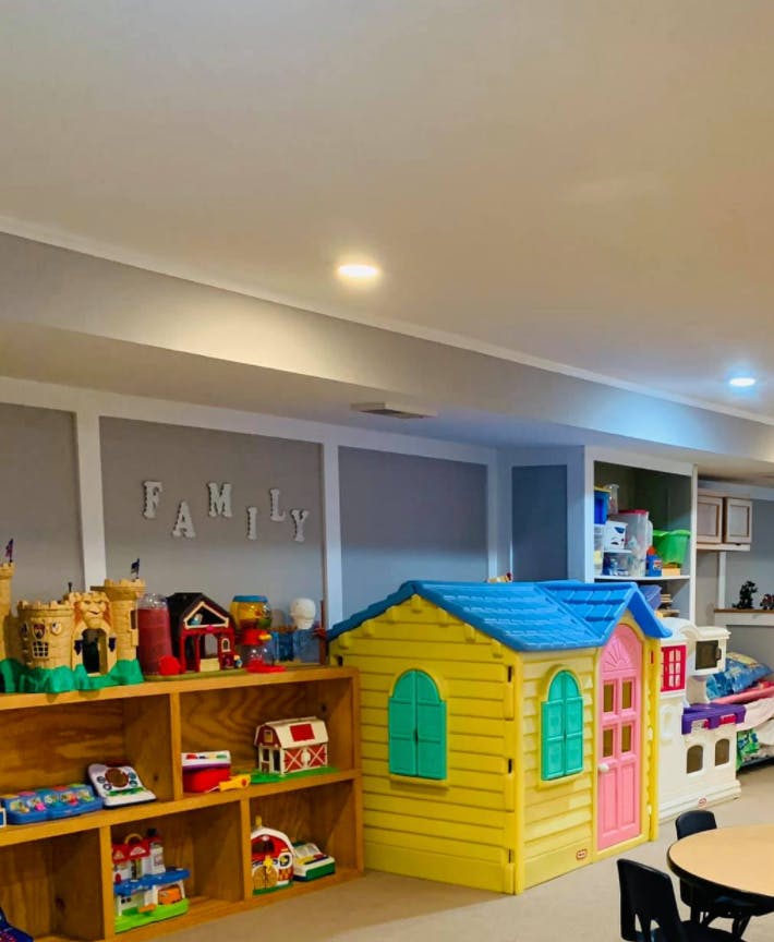 Playroom with toy house, shelves of toys, and a table with "FAMILY" on the wall