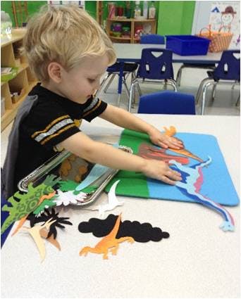Child playing with dinosaur cutouts on a table in a classroom