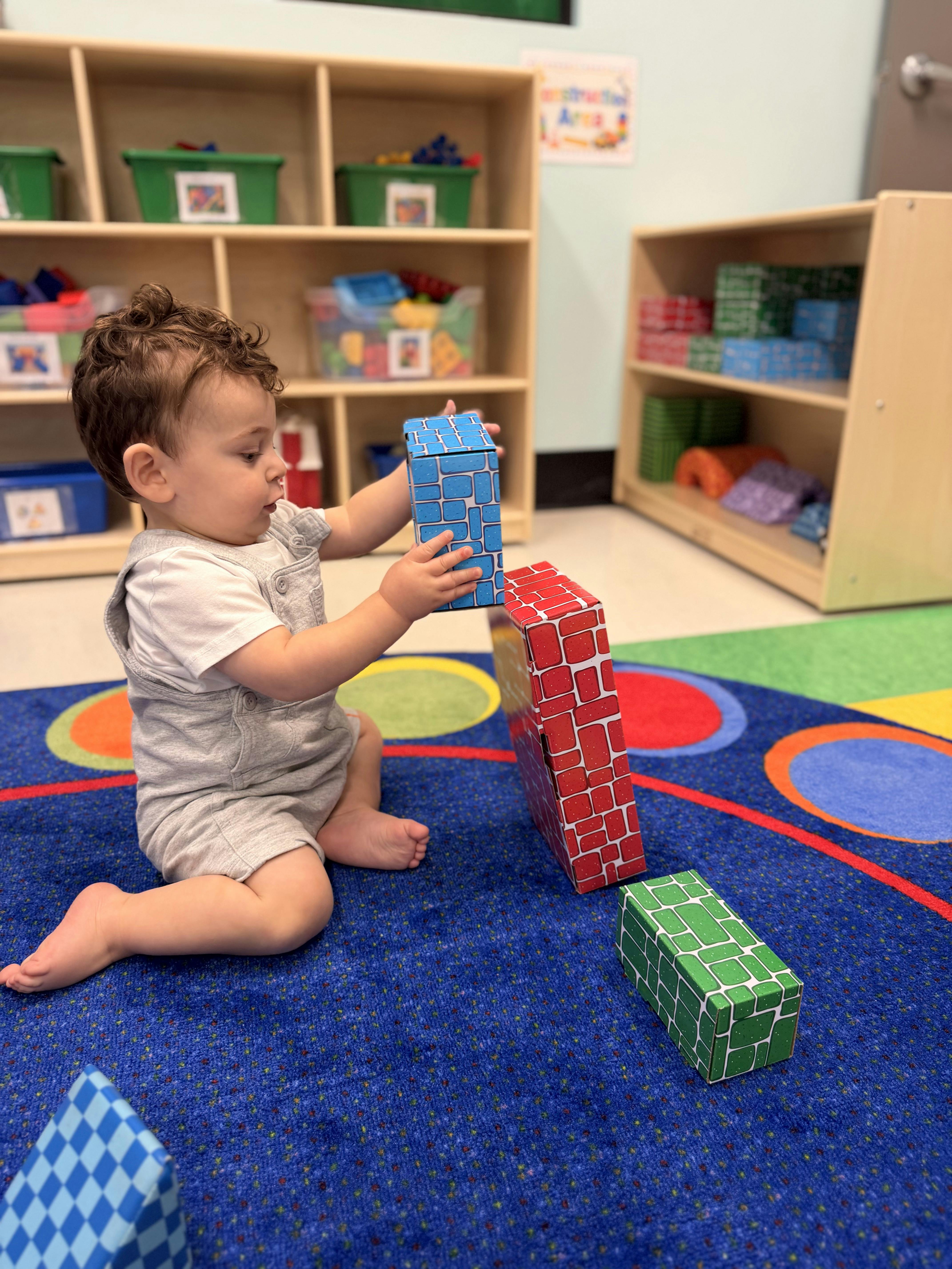 Child playing with large building blocks on a rug in a classroom