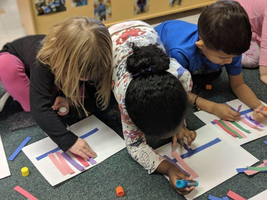 Three children on the floor doing crafts with paper and glue