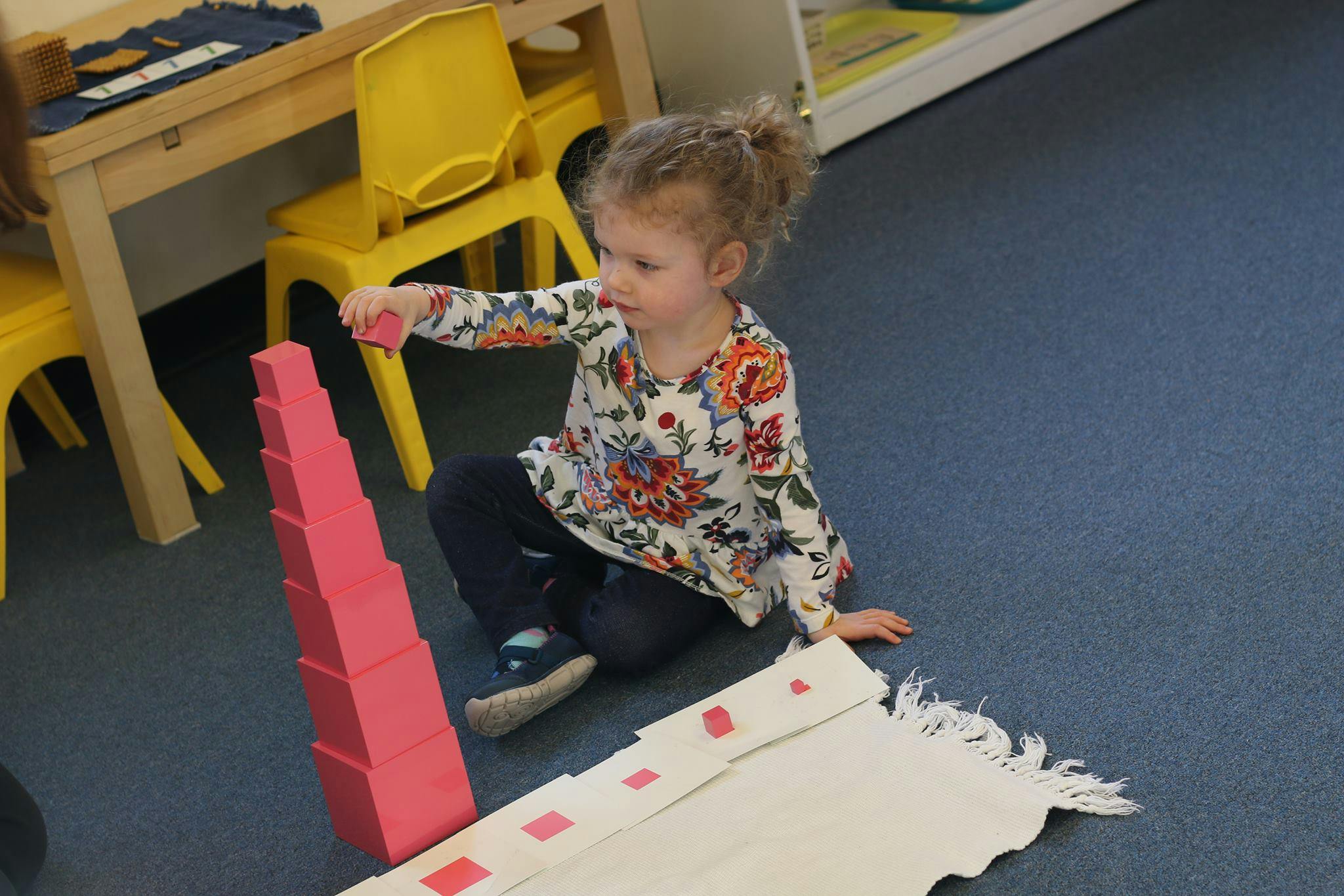 Child building a tower with pink blocks on the floor