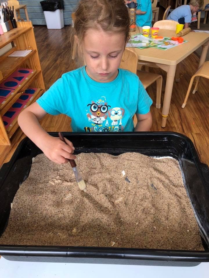Child using a brush in a tray of sand