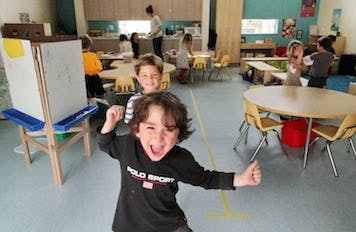 Child smiling and gesturing thumbs up in a classroom