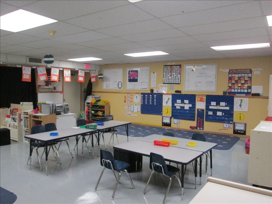 Empty classroom with small tables and chairs, and learning materials on the walls
