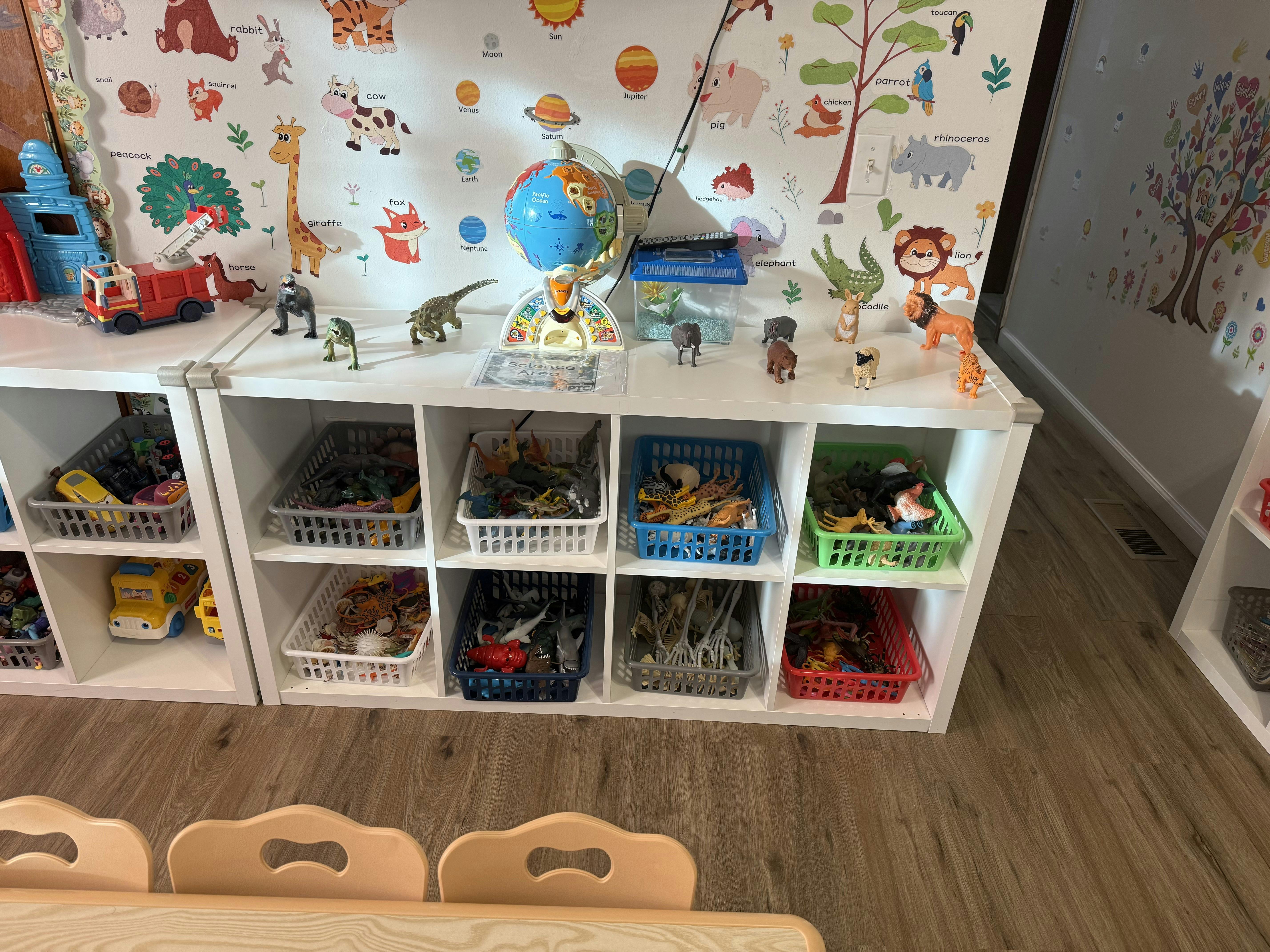 White storage cubbies filled with baskets of toys below a wall with animal and planet stickers