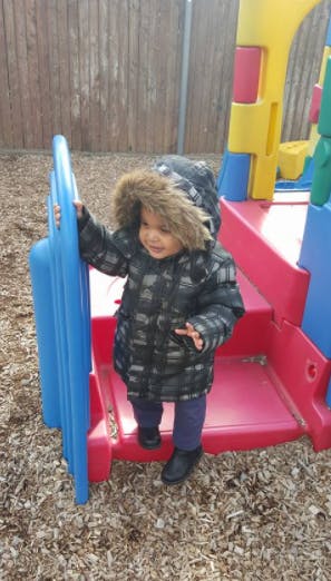 Child in a winter coat standing on a playground structure