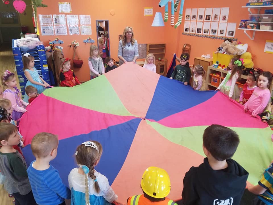 Adult and children playing with a colorful parachute in a room