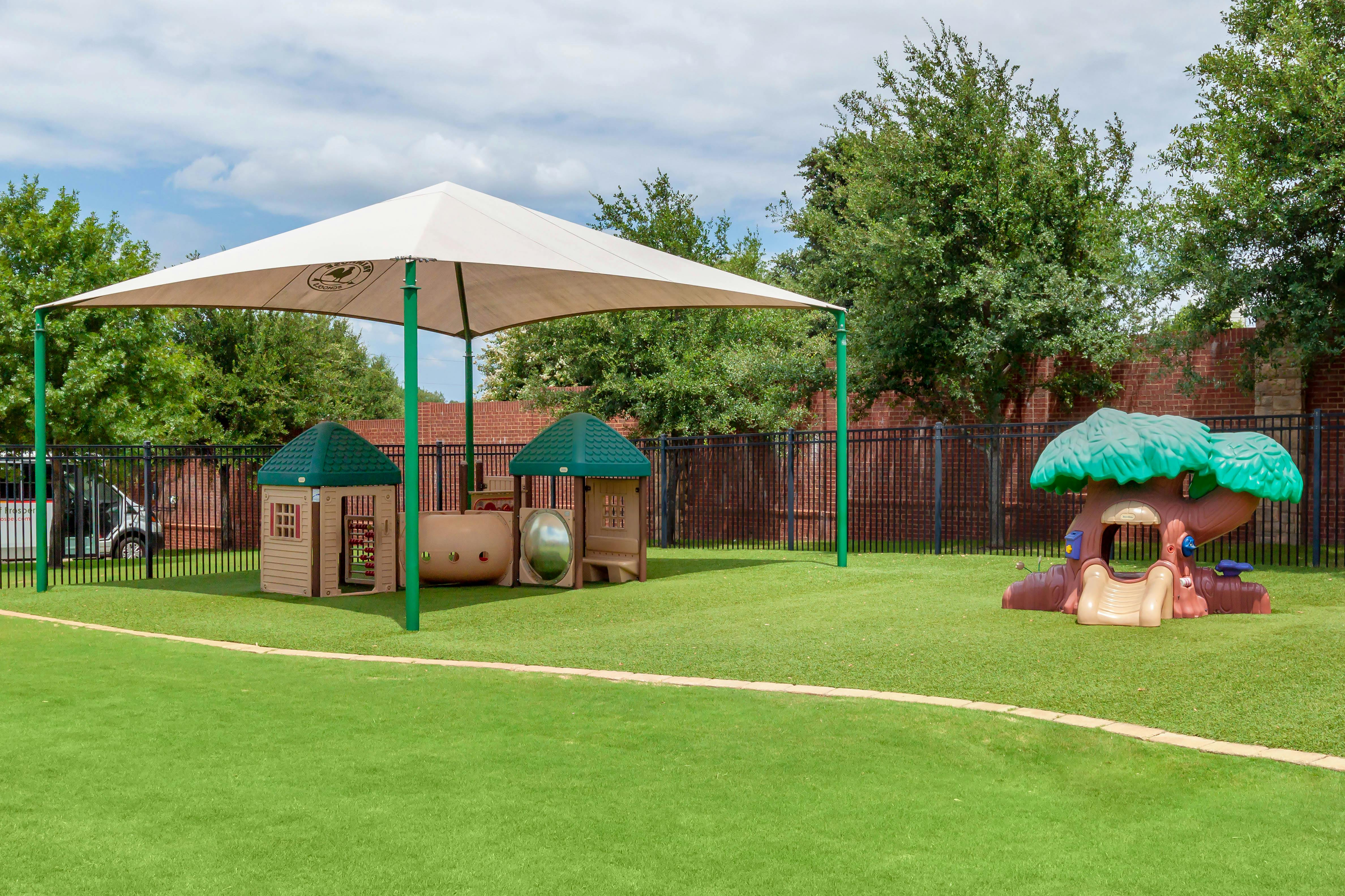 Playground with shade structure, two playhouses, and a tree-themed climbing structure