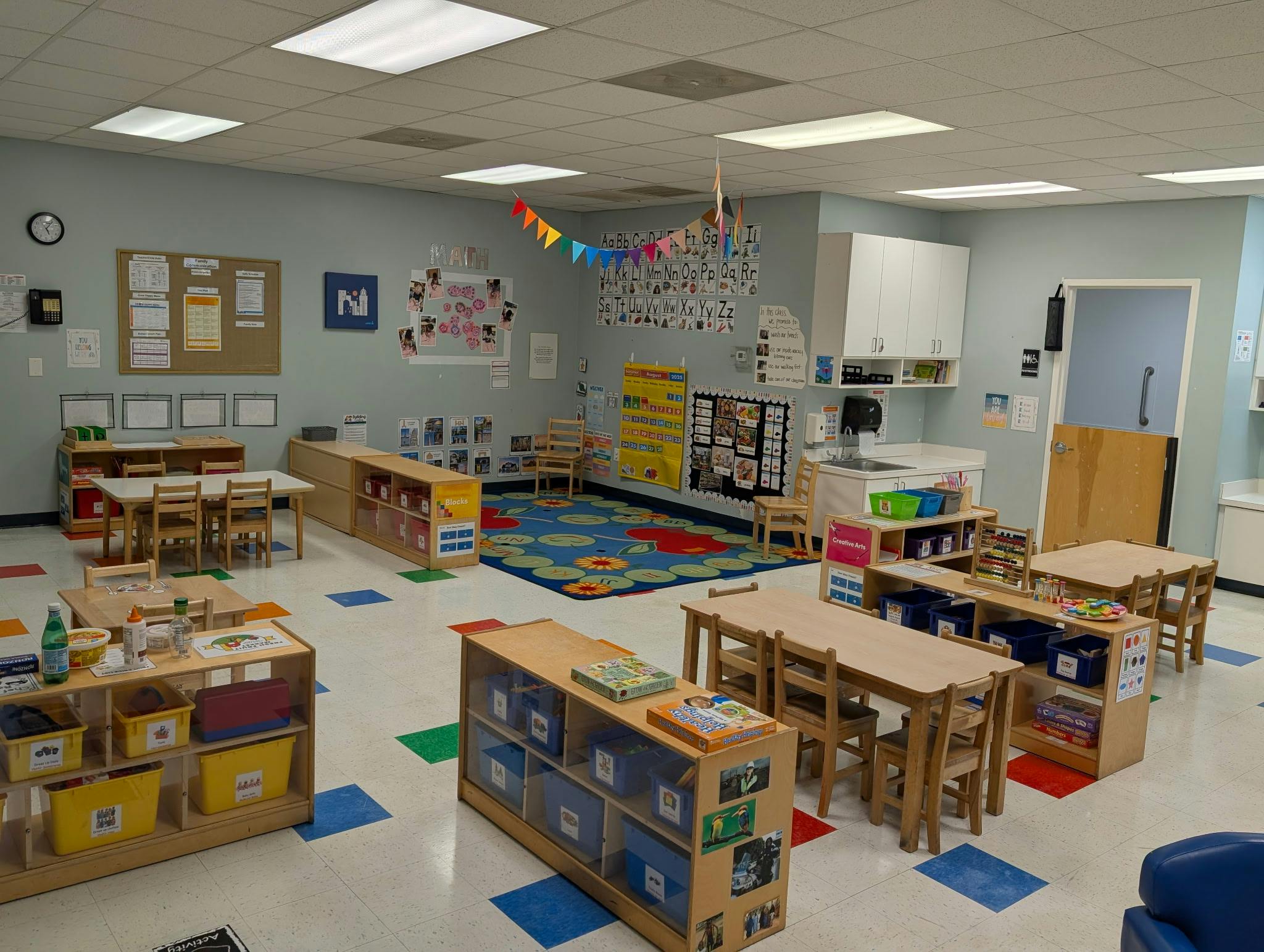 An empty early childhood classroom with multiple small tables, chairs, and learning centers