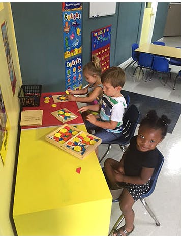 Children playing with shape puzzles at a table in a classroom