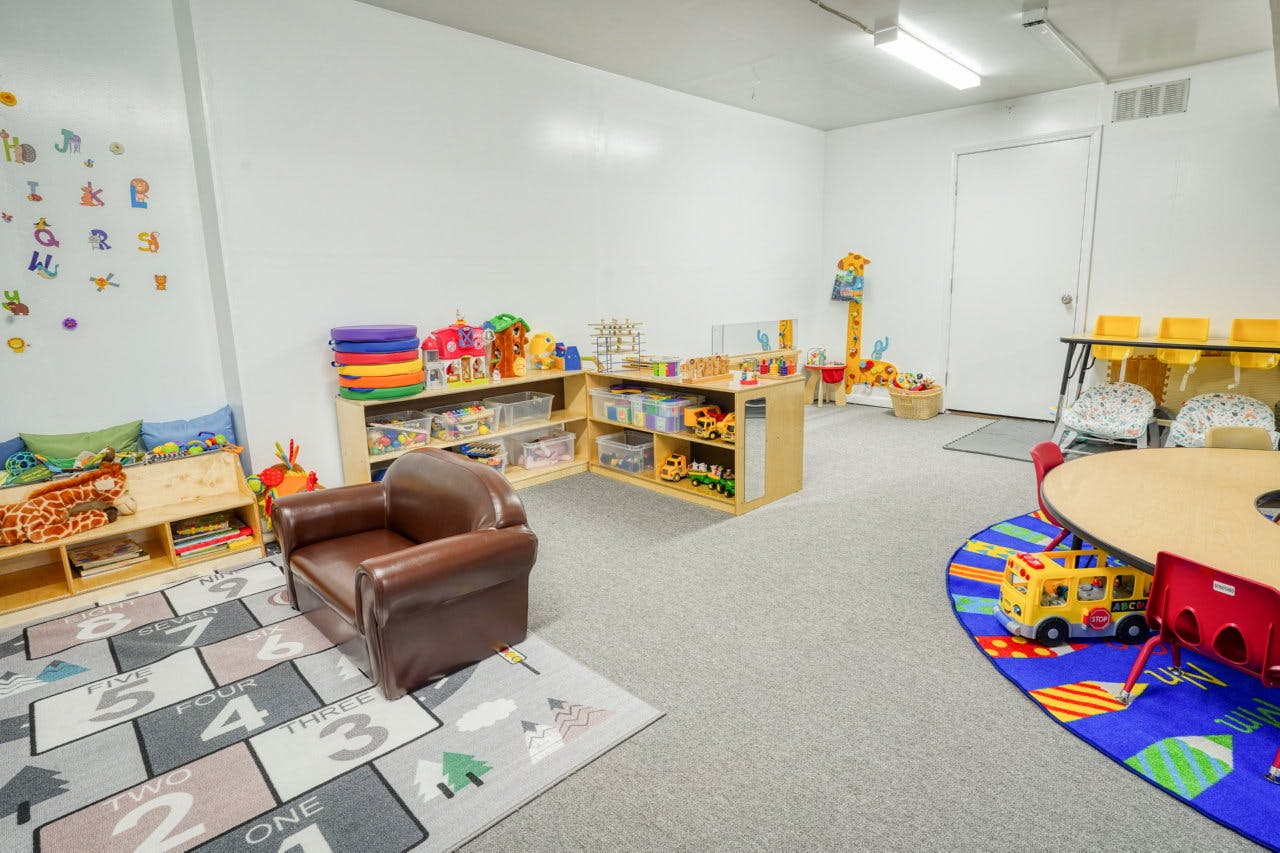 Playroom with shelves of toys, a small armchair, and a round table with chairs