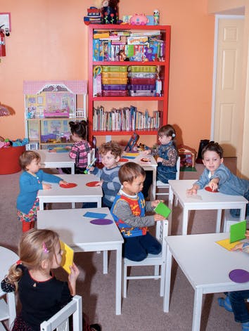Children sitting at tables in a classroom, playing with paper shapes