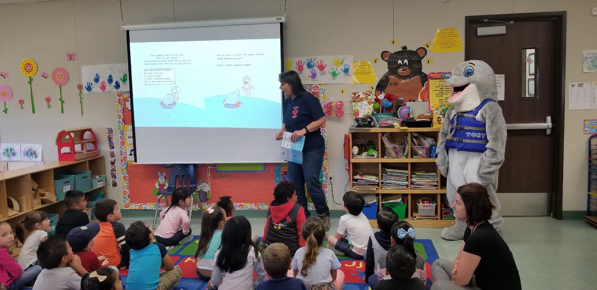 Adult presenting to children and a person in a mascot costume in a classroom