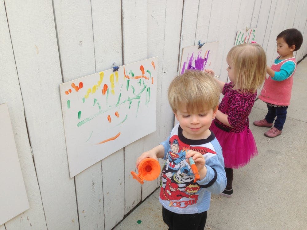 Three children painting on paper attached to a wall