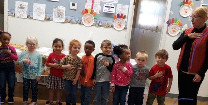 Adult and children standing with hands over hearts in a classroom