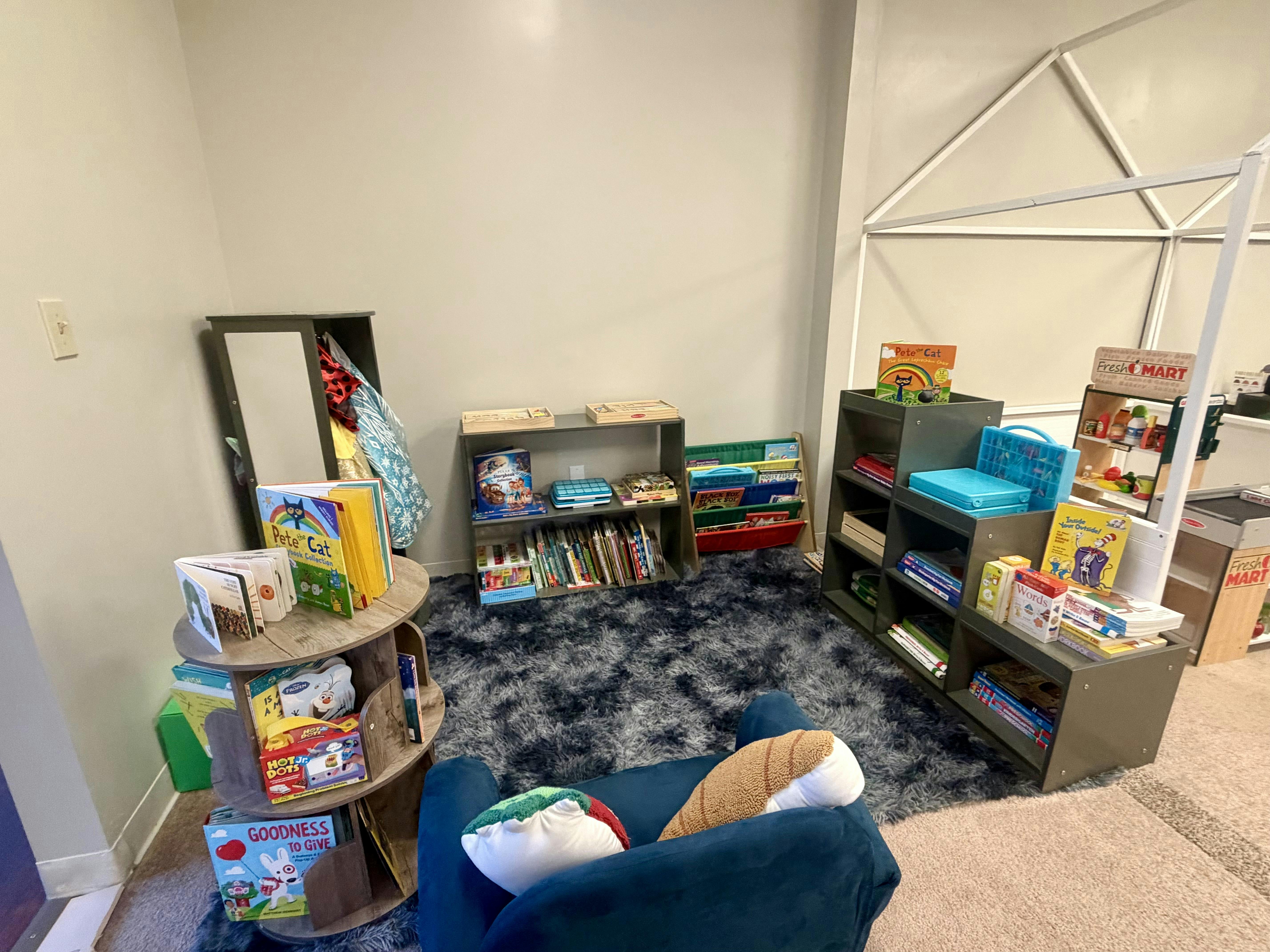 A children's reading nook with shelves of books, a soft chair, and a fluffy rug