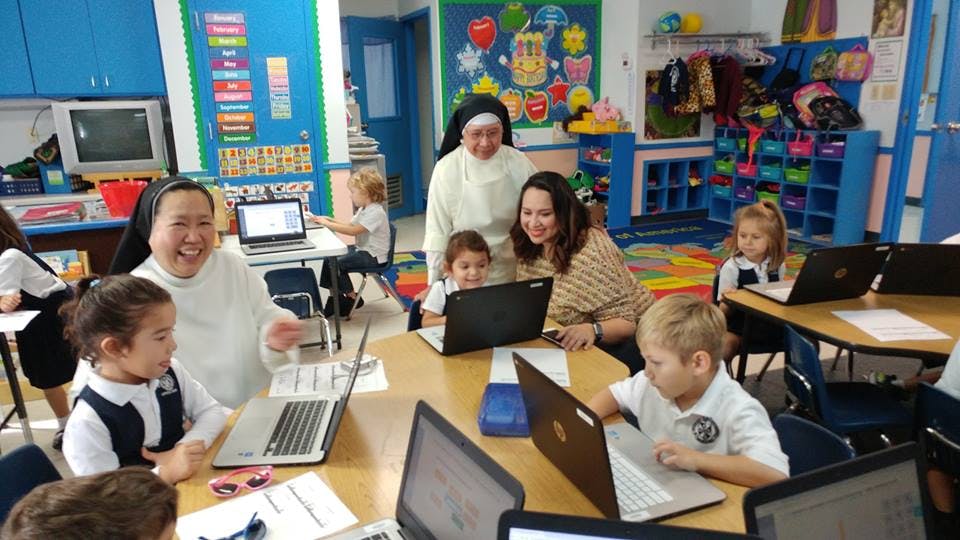 Adults and children using laptops in a classroom