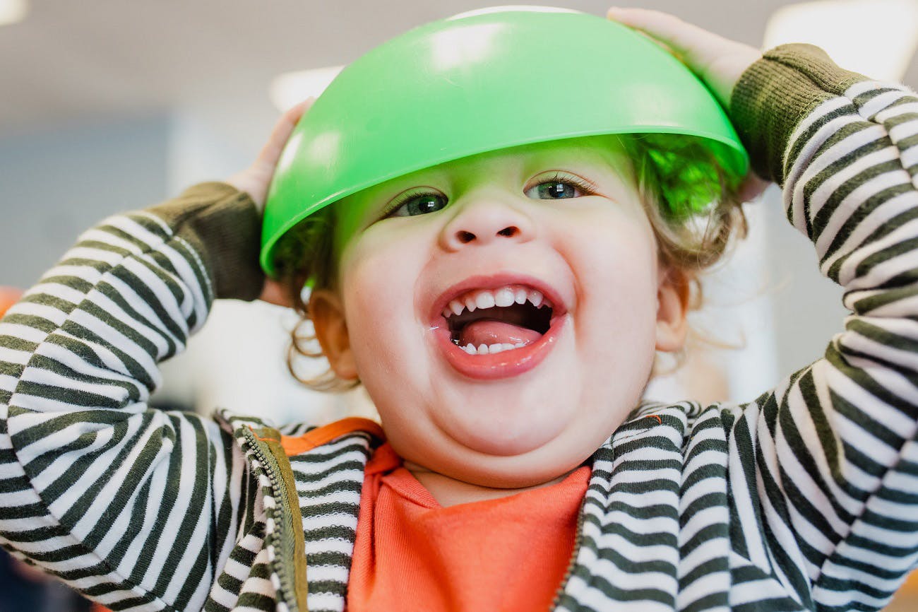 Child with a green bowl on their head