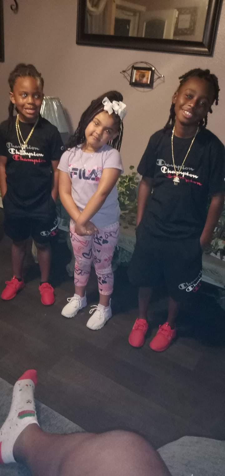 Three children standing together, two wearing black shirts and one wearing a purple shirt
