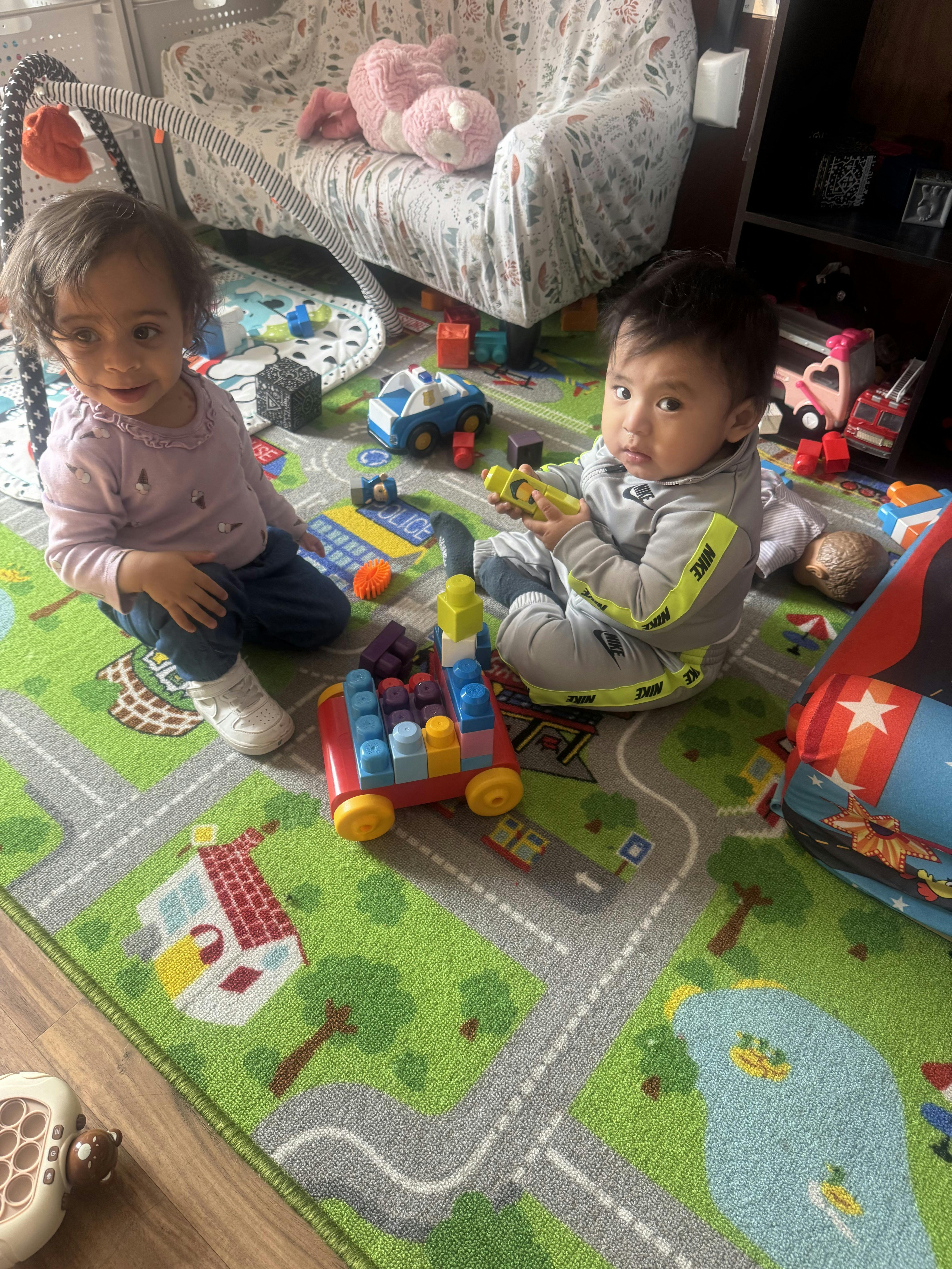 Two children sitting on a play mat with colorful building blocks
