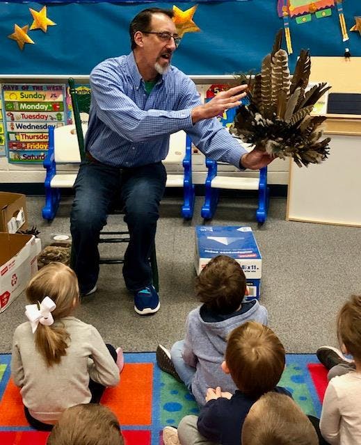 Person holding a bundle of feathers, speaking to children in a classroom