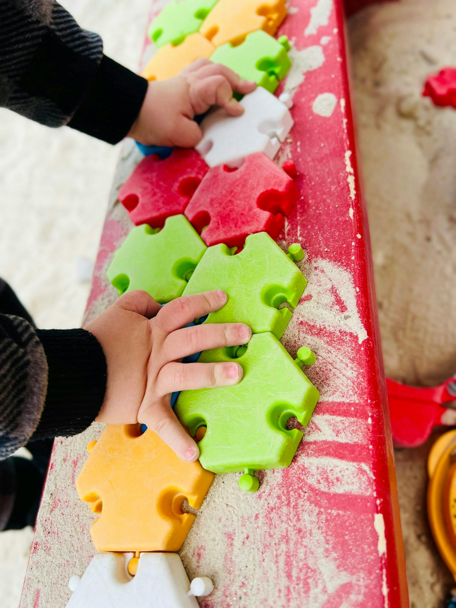 Child's hands playing with colorful puzzle pieces in a sandbox