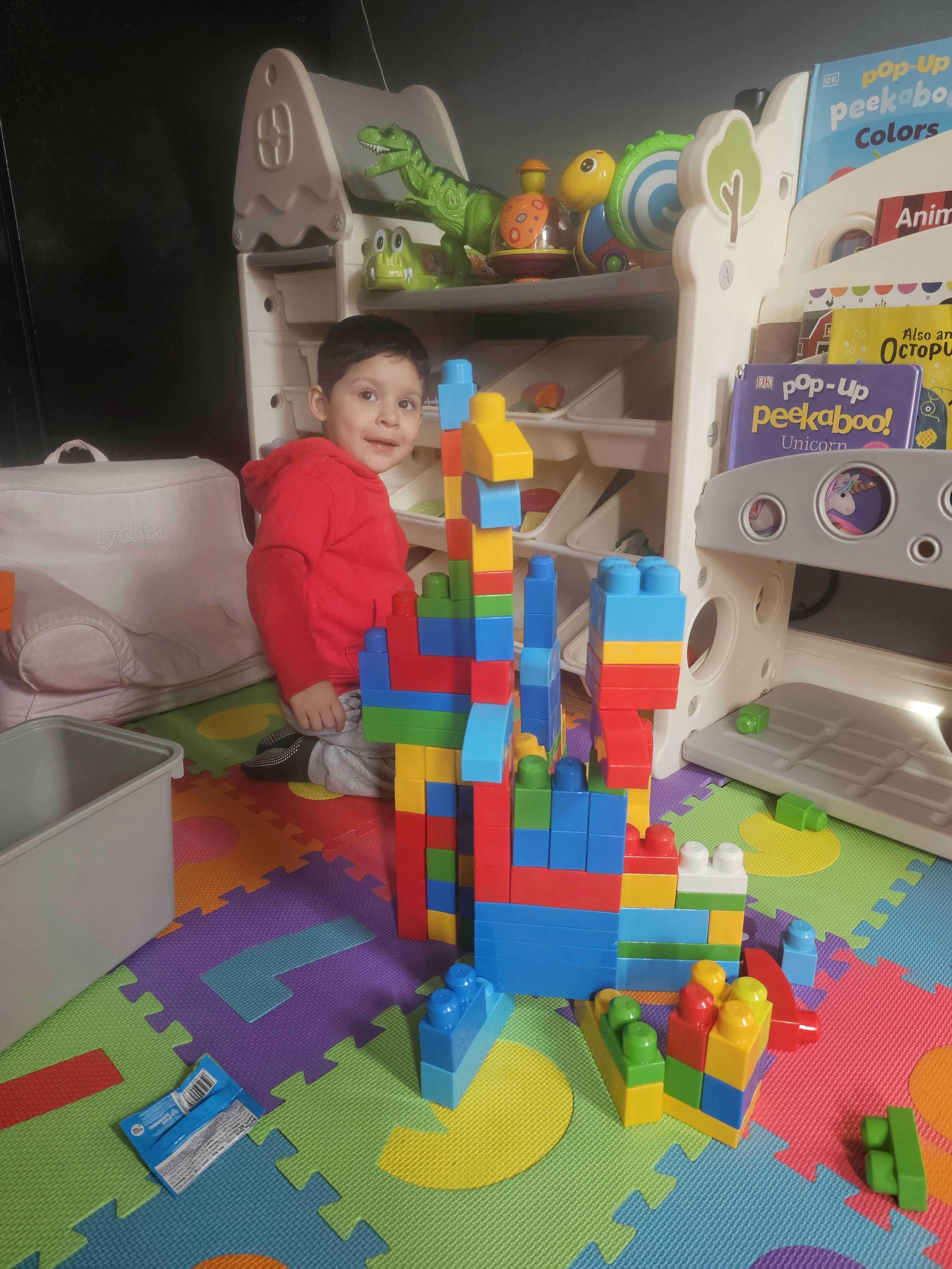 Child lying on a colorful mat next to a large structure made of building blocks