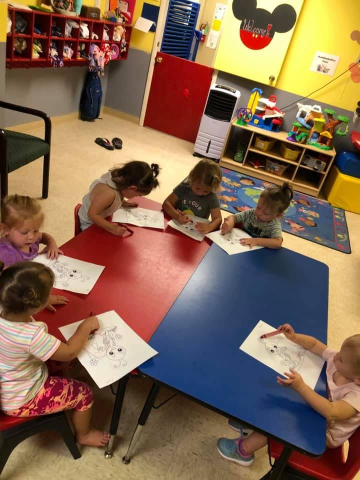 Children sitting at tables coloring pictures in a classroom