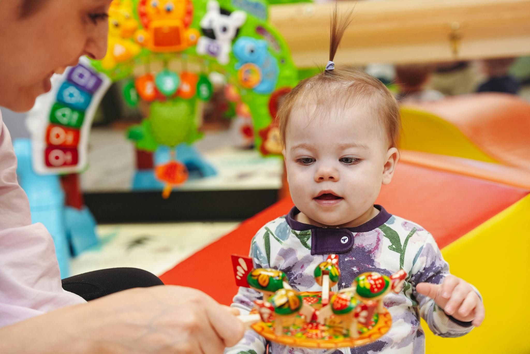 Person holding a toy for a child in a play area