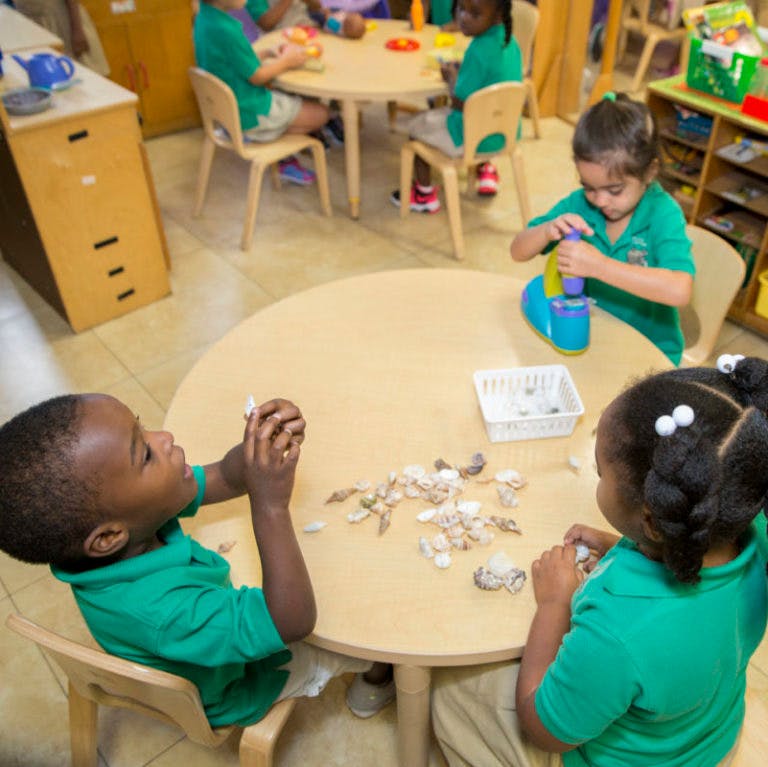Children playing with objects at round tables in a classroom