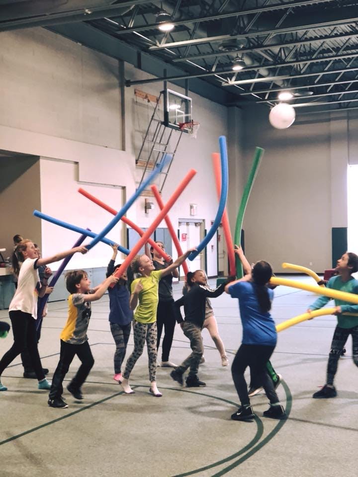 Children playing with colorful pool noodles in a gymnasium