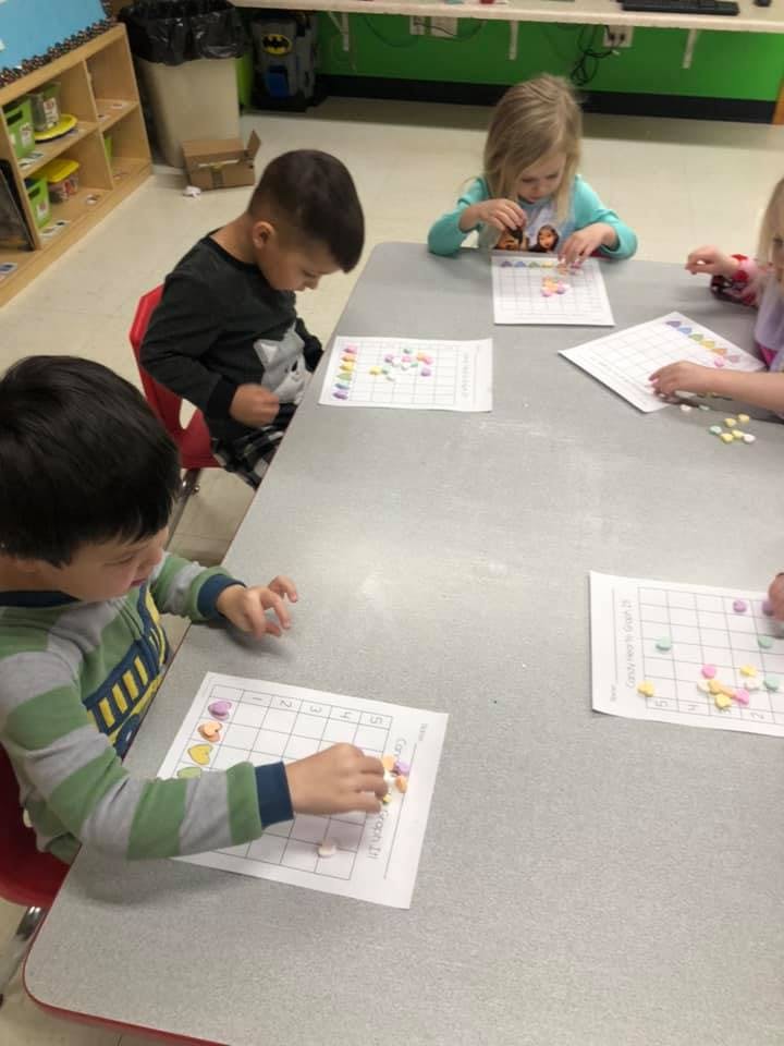 Children at a table placing small objects on papers with papers with grid patterns