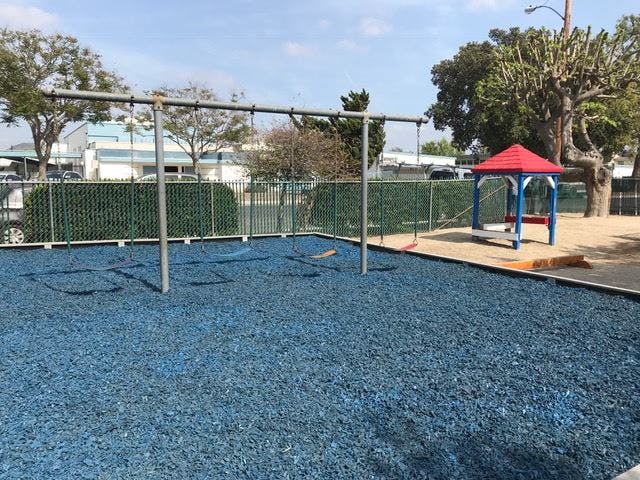 Empty playground with blue ground cover, swing set, and red-roofed gazebo